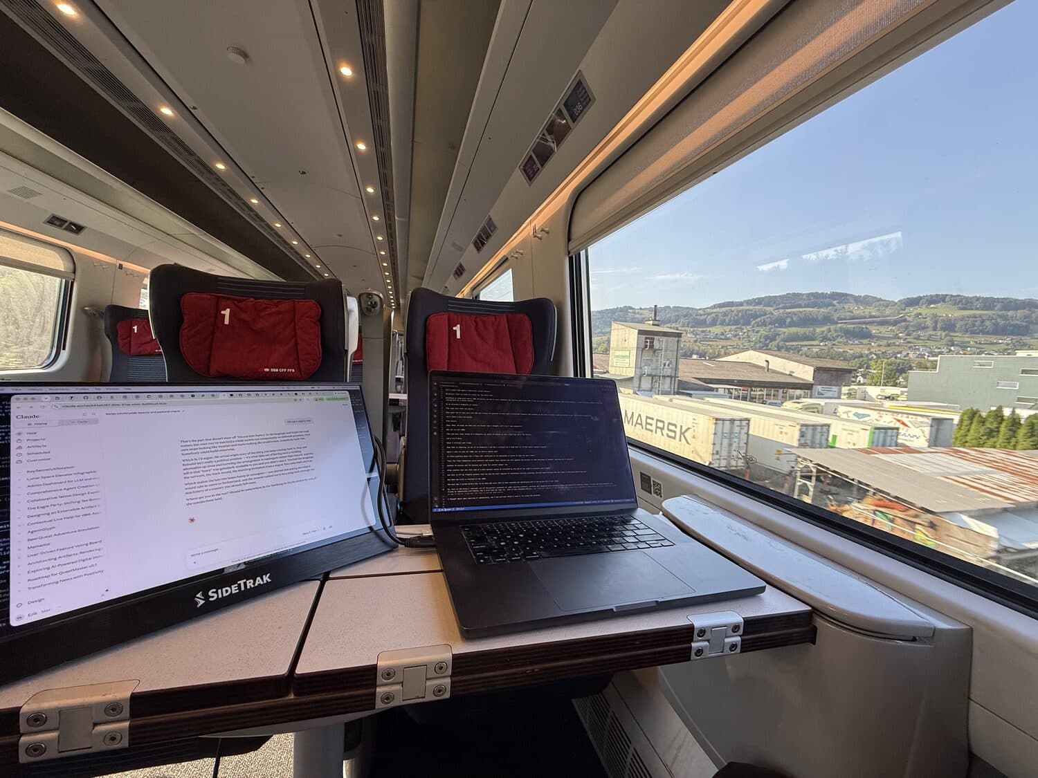 A laptop open on a train table, countryside sliding past the window